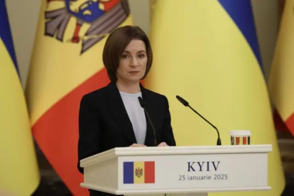 Майя Санду під час прес-конференції перед мікрофонною стійкою. На задньому плані великі прапори Молдови та України.