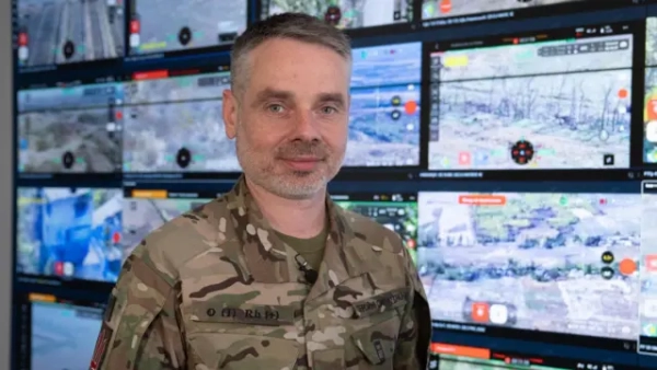 Автор фото, Serhiy Beskrestnov Юрій Мироненко стоїть у військовій формі перед стіною екранів, на яких показані поля, чагарники та кілька будівель. Всі кадри з російсько-українського фронту