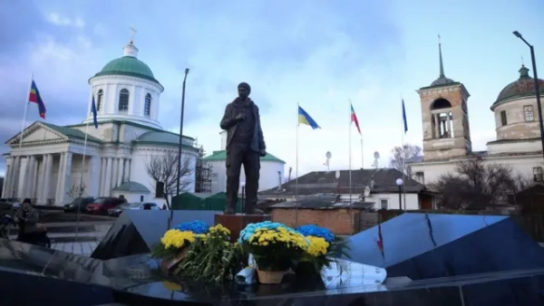Постамент чоловікові в армійському однострої, перед яким покладені квіткові композиції з жовтих і блакитних кольорів. На задньому плані – православні храми із зеленими банями та дзвіницею. Над ними розвіваються декілька стягів, серед яких виразно помітні українські та європейські. Небо вкрите хмарами, але крізь них пробивається світло