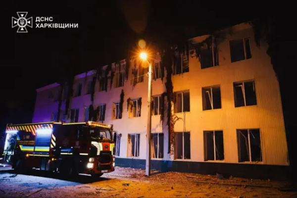 Біла триповерхова споруда з побитими вікнами. Біля неї розміщена пожежна машина