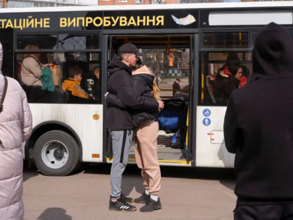 Молода пара в спортивному одязі та чорних куртках обіймається на фоні сучасного міського автобуса 