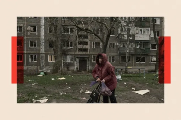 Жінка з сіткою картоплі та сумочкою на фоні будинку зі слідами обстрілів